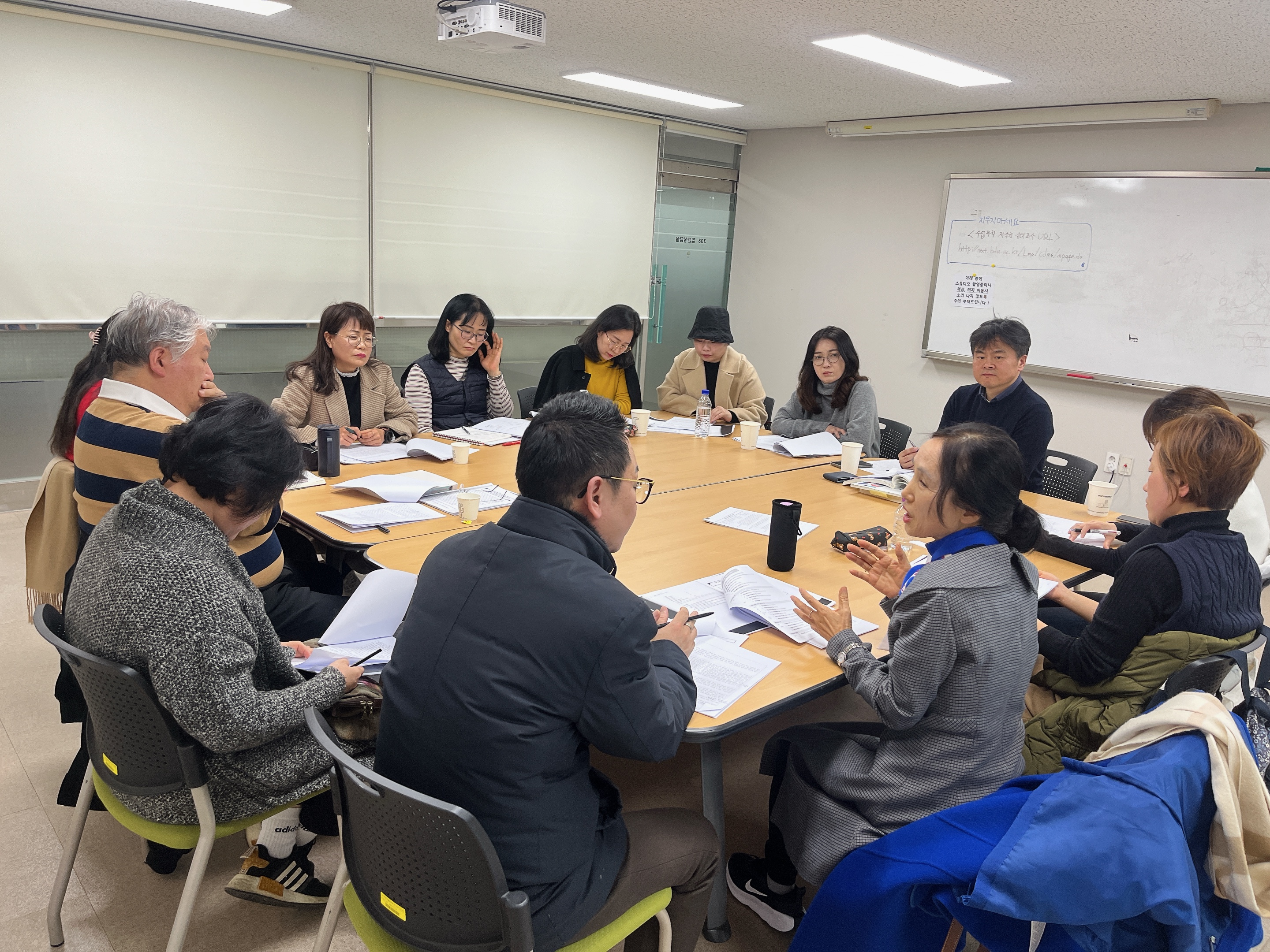 대학원수련상담원 수련(12/06). 대화를 나누고 있는 학생 두 명과 그 모습을 보고 있는 사람들